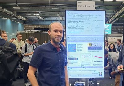 A male researcher stands in front of a large digital screen with a scientific poster