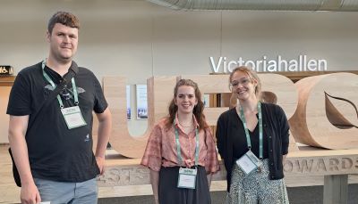 Three young scientists standing in front of a carved wooden 'IUFRO' sign