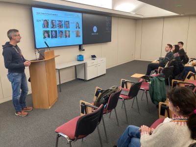 A speaker at a lectern showing slides in a lecture room.