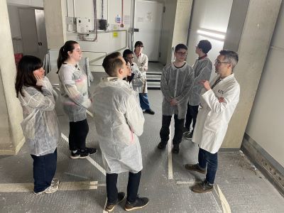 A group of interns wearing lab coats and listening to an expert speak.