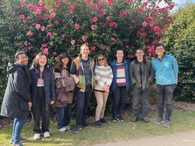 A group of interns pose for a photograph in a garden with pink blossoms behind them.